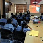 Students in a classroom with a teacher presenting a lecture.